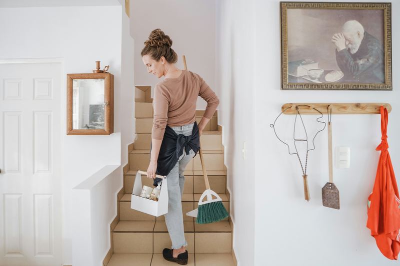 A home helper carrying cleaning supplies and a broom up the stairs